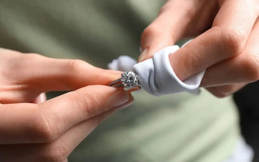 Hands gently cleaning a sparkling diamond engagement ring with a soft white polishing cloth.