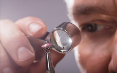 A jeweler uses a professional loupe and stone holder to closely inspect a faceted pink gemstone.