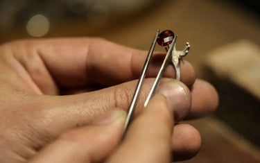Close-up of a jeweler using precision tweezers to carefully position a red gemstone onto a silver ring setting.
