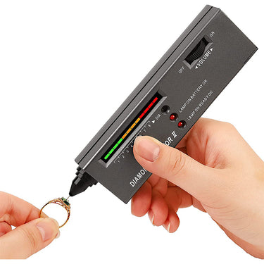 Diamond Selector II electronic tester probe touching a green gemstone on a gold ring to verify authenticity.