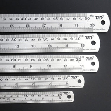 Five stainless steel rulers of varying lengths stacked horizontally from largest to smallest.