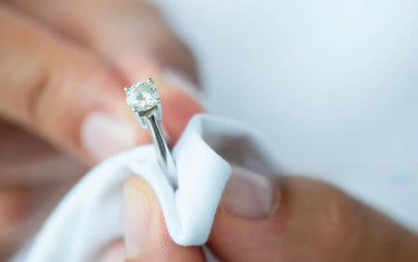 Close-up of hands gently polishing a diamond solitaire engagement ring with a soft white cleaning cloth.