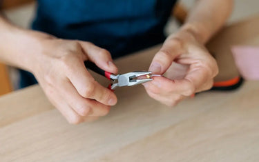 A craftsperson using chain nose pliers to carefully work with a small metal component for jewelry making.