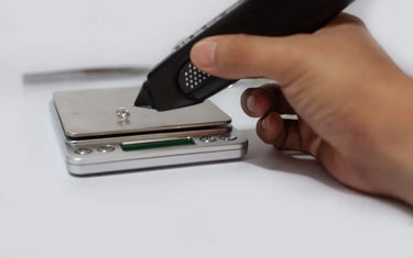A jeweler uses a selector pen to test a loose gemstone placed on a digital carat scale.