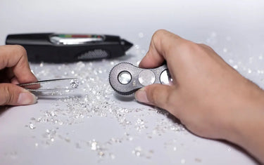 A jeweler uses tweezers and a loupe to inspect loose diamonds on a white surface.
