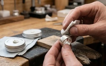 Jeweler manually polishing a silver ring using a soft cloth and fine polishing compound on a bench pin.