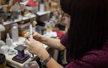 A jeweler checking a ring size on a metal ring mandrel stick in a workshop.