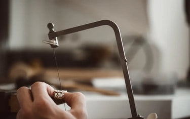 Close-up of a bench jeweler carefully cutting a detailed gold ring with a professional piercing saw frame.