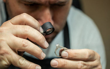 Professional jewelry repair technician inspecting a diamond ring with a hand-held loupe.