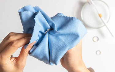 Overhead view of hands using a blue microfiber cloth to clean a silver diamond ring.