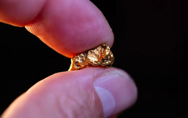 Close up view of a raw natural gold nugget held between fingers