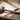 Rawhide mallet lying on a sheet of silver metal with strips and jewelry-making tools on a wooden workbench.