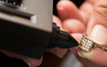 Jeweler using an electronic diamond tester pen to test pave set stones on an earring