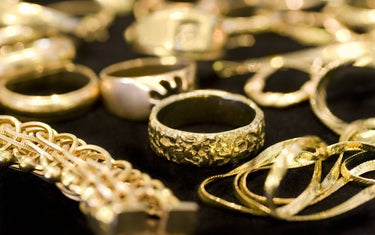 A collection of various gold jewelry including textured rings and intricate chains on a dark background.