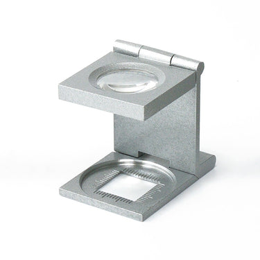 Side-angled view of a silver folding linen tester loupe showing the calibrated measurement window on the base.