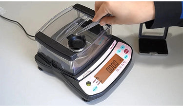 Using tweezers to place a diamond into the gem tray of the MR-260C carat scale with windshield.