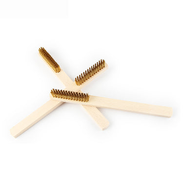 Three straight wooden handle brass wire cleaning brushes crossed over one another on a seamless white surface.