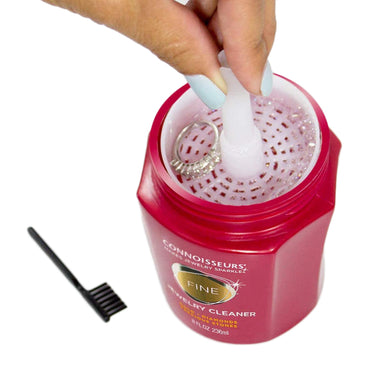 A hand using the dip tray and brush to clean a diamond ring inside the Connoisseurs Fine Jewelry Cleaner jar.