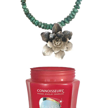 A tarnished silver flower pendant on a turquoise bead necklace shown above the Connoisseurs Silver Cleaner jar.