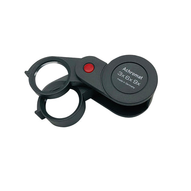 Top-down view of the Eschenbach Achromat folding loupe with red pivot button and "made in Germany" branding.
