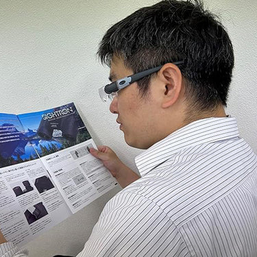 A man wearing MaxDetail loupes to read a technical document, demonstrating hands-free magnification.