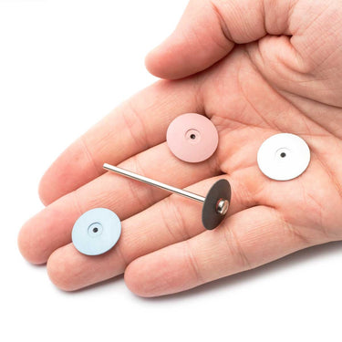 A hand holding four lens polishers, with a black wheel mounted onto a screw-type mandrel pin.