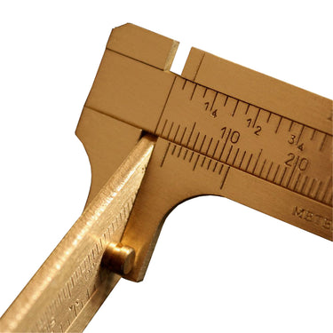 Macro close-up shot focusing on the engraved fraction markings and slider button of a brass caliper.