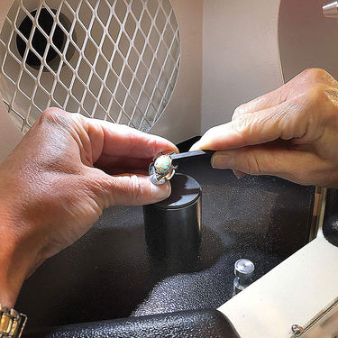 Close-up view of hands setting a gemstone ring inside the Foredom lighted work chamber.