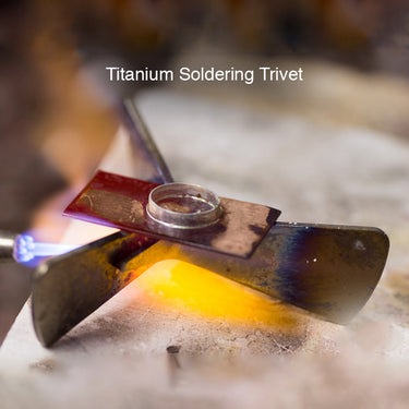 A jewelry torch flame heating a copper bezel piece supported by a glowing titanium soldering trivet