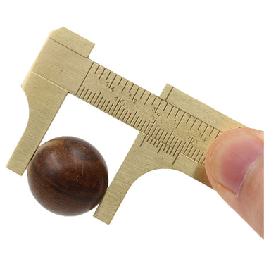 A hand using a mini brass sliding caliper to measure the outer diameter of a small dark wooden bead.