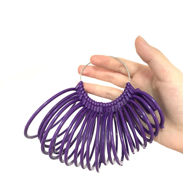 A hand holding the wire loop of a purple plastic bangle sizer tool to display the sizing rings.