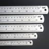 Five stainless steel rulers of varying lengths stacked horizontally from largest to smallest.