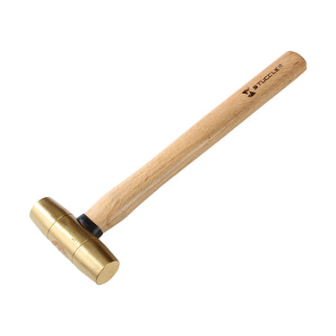 High angle view of a Stuccler brass mallet placed diagonally, pointing towards the top right.