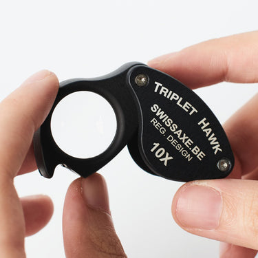 SwissAxe Triplet Hawk 10X loupe held between fingers to show its ergonomic grip for diamond inspection.